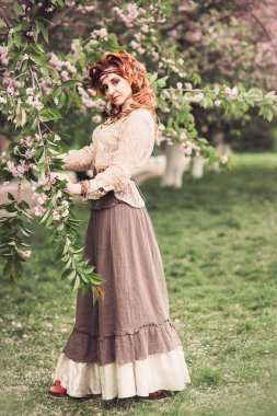 Kiraz çiçekleri ağacın altında bahar Parkı duran güzel kızıl saçlı kadın. Görüntü tonda. Verticalbeautiful Kızıl saçlı kadın bahar zaman çiçeği ağacının altında