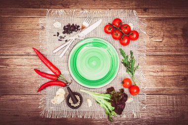 Taze domates, biber ve diğer baharatlar ve otlar ahşap masa ve bez peçete merkezinde modern ışık yeşil plaka çevresinde. Üstten Görünüm. Metniniz için boş yer. Yatay.