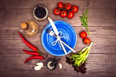 Taze domates, biber ve diğer baharatlar ve otlar ahşap masa merkezinde modern mavi plaka çevresinde. Üstten Görünüm. Çatal ve bıçak plaka üzerinde. Yatay.