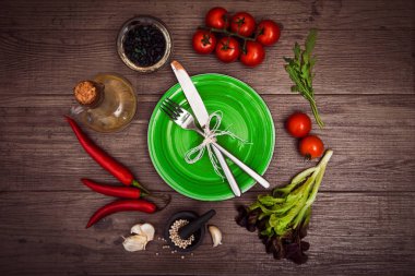 Taze domates, biber ve diğer baharatlar ve otlar ahşap masa merkezinde modern yeşil plaka çevresinde. Üstten Görünüm. Çatal ve bıçak plaka üzerinde. Yatay.
