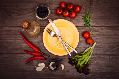 Taze domates, biber ve diğer baharatlar ve otlar ahşap masa merkezinde modern sarı plaka çevresinde. Üstten Görünüm. Çatal ve bıçak plaka üzerinde. Yatay.