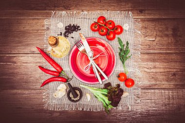 Taze domates, biber ve diğer baharatlar ve otlar ahşap masa ve bez peçete merkezinde modern kırmızı plaka çevresinde. Çatal ve bıçak plaka üzerinde bağlı. Üstten Görünüm. Yatay.