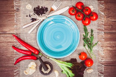 Taze domates, biber ve diğer baharatlar ve otlar ahşap masa ve bez peçete merkezinde modern ışık mavi plaka çevresinde. Üstten Görünüm. Metniniz için boş yer. Yakın çekim.