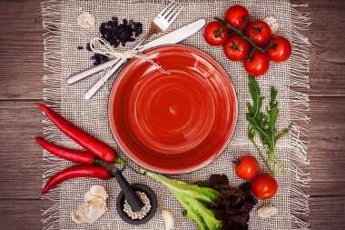 Taze domates, biber ve diğer baharatlar ve otlar ahşap masa ve bez peçete merkezinde modern kırmızı plaka çevresinde. Üstten Görünüm. Metniniz için boş yer. Yakın çekim.