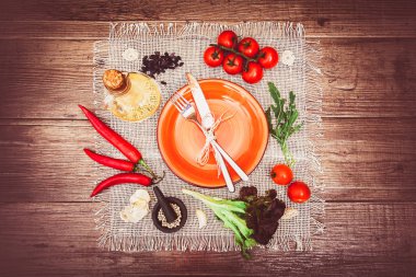 Taze domates, biber ve diğer baharatlar ve otlar ahşap masa ve bez peçete merkezinde modern turkuaz plaka çevresinde. Çatal ve bıçak plaka üzerinde bağlı. Üstten Görünüm. Yatay.