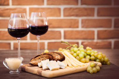 Peynir, kahverengi ekmek, iki bardak kırmızı şarap. Yatay.