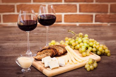 Peynir, kahverengi ekmek, iki bardak kırmızı şarap. Yatay.