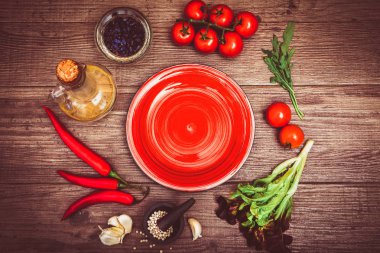 Taze domates, biber ve diğer baharatlar ve otlar ahşap masa ve bez peçete merkezinde modern kırmızı plaka çevresinde. Üstten Görünüm. Metniniz için boş yer. Yakın çekim.
