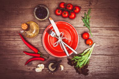 Taze domates, biber ve diğer baharatlar ve otlar ahşap masa merkezinde modern kırmızı plaka çevresinde. Üstten Görünüm. Çatal ve bıçak plaka üzerinde. Yatay.