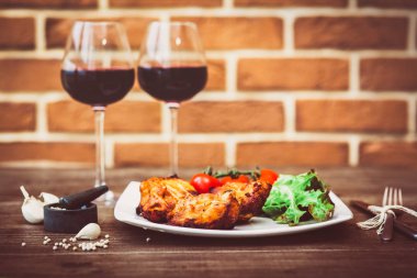 Sulu ızgara et fileto parçalarını kiraz domates şube ve marul üzerine beyaz tabak, bardak kırmızı şarap, bıçak, çatal, tuğla duvar arka plan üzerinde hizmet verdi. Romantik kavramı. Yatay