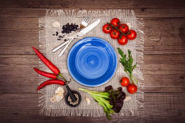 Taze domates, biber ve diğer baharatlar ve otlar ahşap masa ve bez peçete merkezinde modern koyu mavi plaka çevresinde. Üstten Görünüm. Metniniz için boş yer. Yatay.