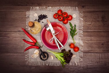 Taze domates, biber ve diğer baharatlar ve otlar ahşap masa ve bez peçete merkezinde modern kırmızı plaka çevresinde. Çatal ve bıçak plaka üzerinde bağlı. Üstten Görünüm. Yatay.