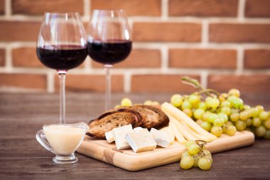 Peynir, kahverengi ekmek, iki bardak kırmızı şarap. Yatay.