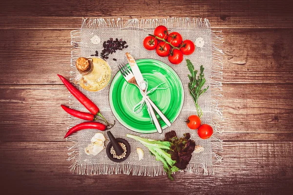 Taze domates, biber ve diğer baharatlar ve otlar ahşap masa ve bez peçete merkezinde modern turkuaz plaka çevresinde. Çatal ve bıçak plaka üzerinde bağlı. Üstten Görünüm. Yatay.