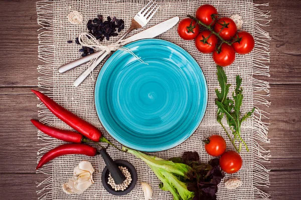 Taze domates, biber ve diğer baharatlar ve otlar ahşap masa ve bez peçete merkezinde modern turkuaz plaka çevresinde. Üstten Görünüm. Metniniz için boş yer. Yakın çekim.