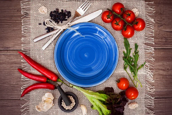 Taze domates, biber ve diğer baharatlar ve otlar ahşap masa ve bez peçete merkezinde modern koyu mavi plaka çevresinde. Üstten Görünüm. Metniniz için boş yer. Yakın çekim.