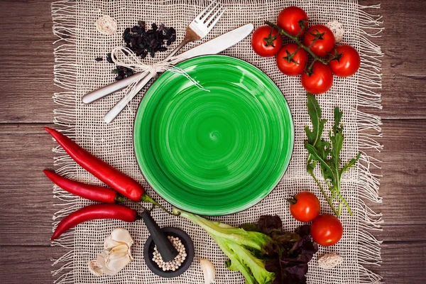 Taze domates, biber ve diğer baharatlar ve otlar ahşap masa ve bez peçete merkezinde modern parlak yeşil plaka çevresinde. Üstten Görünüm. Metniniz için boş yer. Yakın çekim.