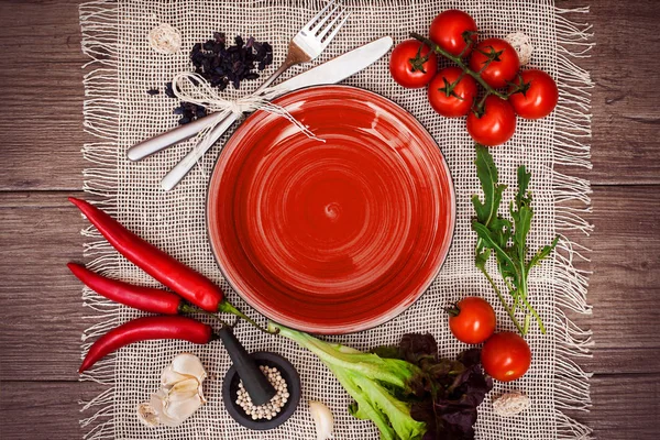 Taze domates, biber ve diğer baharatlar ve otlar ahşap masa ve bez peçete merkezinde modern kırmızı plaka çevresinde. Üstten Görünüm. Metniniz için boş yer. Yakın çekim.