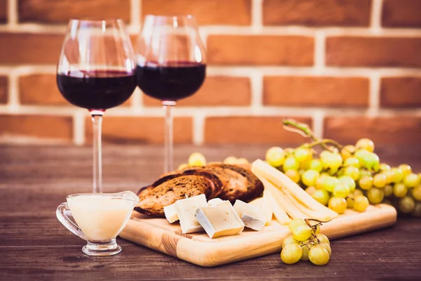 Peynir, kahverengi ekmek, iki bardak kırmızı şarap. Yatay.