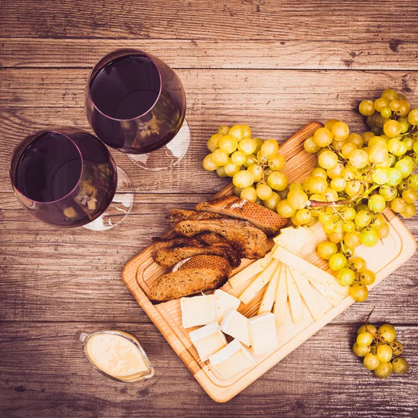 Peynir, kahverengi ekmek, iki bardak kırmızı şarap. Yatay.