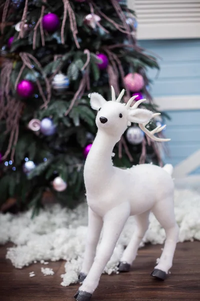 White deer toy near Christmas tree with unusual ornament. — Stock Photo, Image