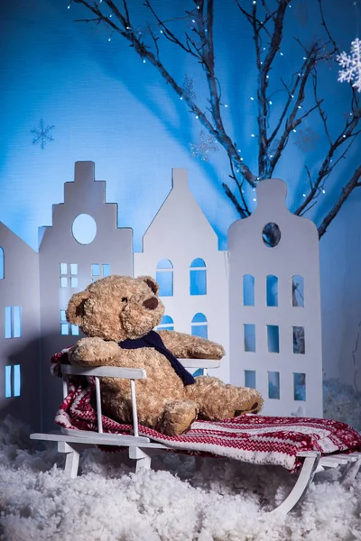 Teddy bear with scarf sitting on a sled among snow at the blue b — Stock Photo, Image