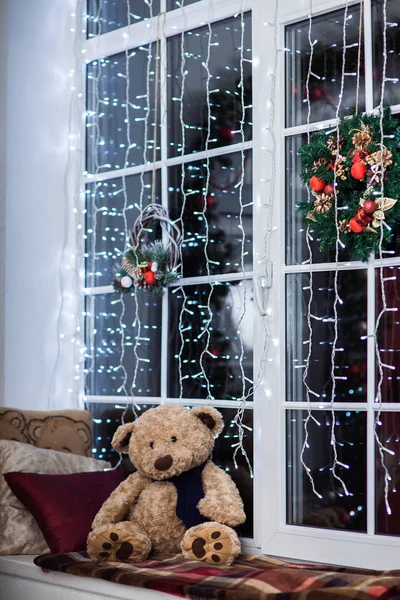 Holiday decoration on the windowsill covered with woolen plaid. Christmas wreath, lights and toys. — Stock Photo, Image