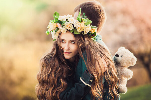 Girl with long wavy hair in a flower wreath hugging her guy. Soft background. Close-up