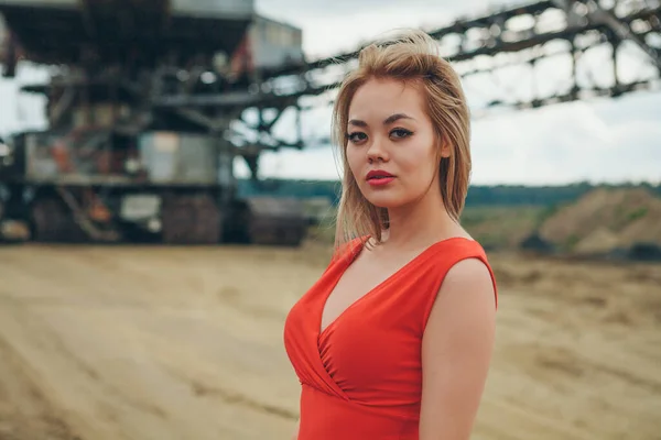 Kırmızı elbiseli güzel Asyalı kadın dev sanayi arka planında poz veriyor.