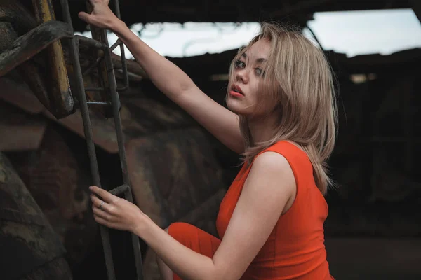 Kırmızı elbiseli genç kadın demir merdivenlere tırmanıyor.