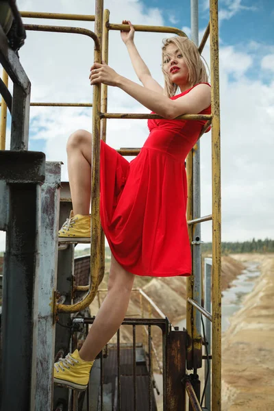 Kırmızı elbiseli genç kadın demir merdivenlere tırmanıyor.