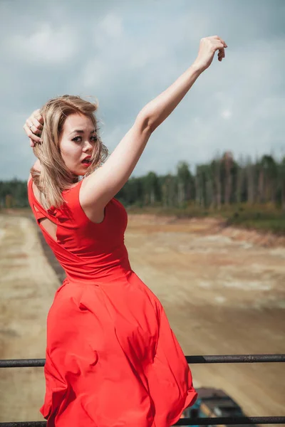 Kırmızı elbiseli genç Asyalı kadın dans ediyor ve el sallıyor.