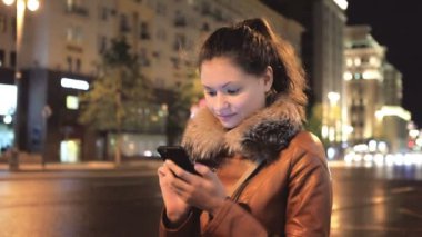 Mutlu kız gece şehrin arka planı Smartphone kullanarak