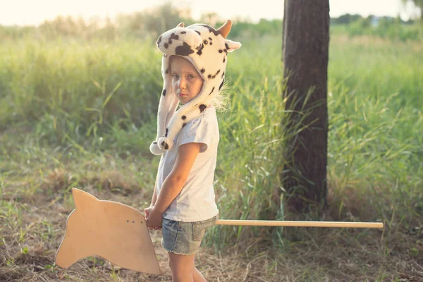 Ребенок в смешной шляпе животного играет с деревянной игрушечной лошадью — стоковое фото