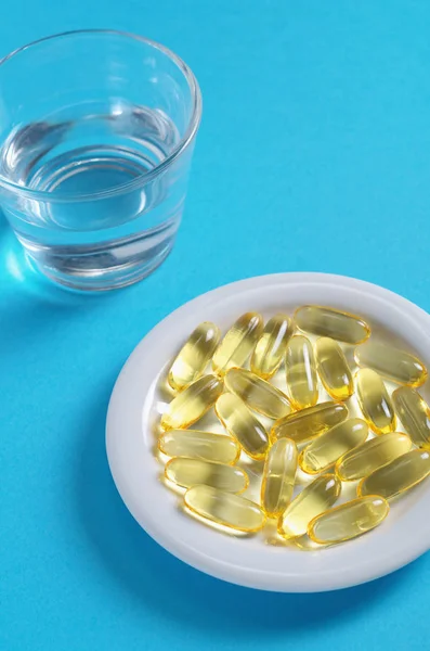 Fish oil capsules and glass of water — Stock Photo, Image