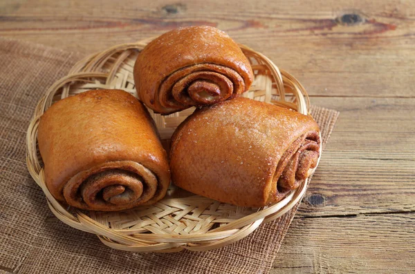 Cinnamon buns on a wicker plate on wooden table close-up