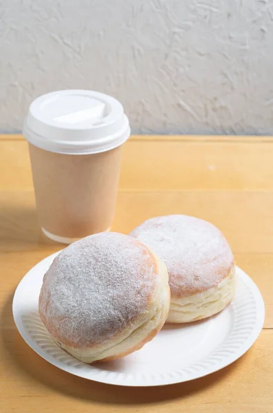 Two donuts on a paper plate and coffee cup on wooden table. Take-away disposable eco dishes