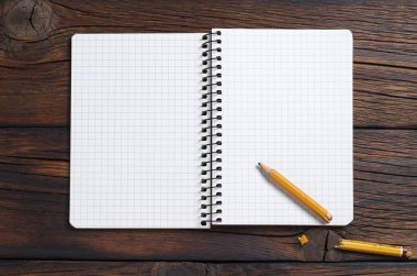 Ahşap zemin üzerinde açık defter ve kırık kalem, üst görünüm
