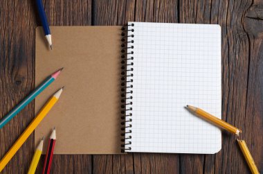 Açılmış defter ve tahta zemin üzerinde çeşitli kalemler, üst görünüm