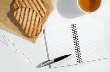 Not defteri, çay fincanı ve ızgara ekmek beyaz masada, üst manzara.