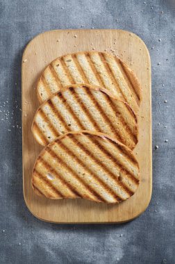 Izgara buğday ekmeği kesim tahtasında gri arka planda, üst manzara