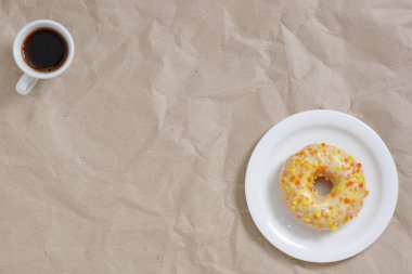 Kremalı ve serpilmiş çörek ve buruşuk kağıttan arka planda bir fincan kahve, fotokopi alanı olan üst manzara.