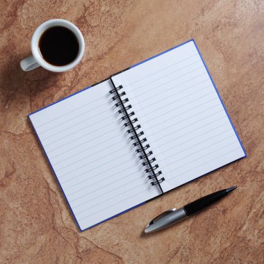 Kalem ve kahve dolu defter taştan arka planda, en üstte. 
