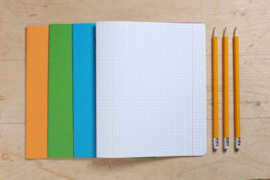 Okul defterleri ve kalemler ahşap arka planda, üst görünümde.