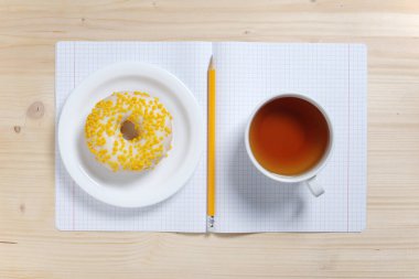 Bir fincan çay, çörek ve okul defterini ahşap masanın üstünde, en üstte.