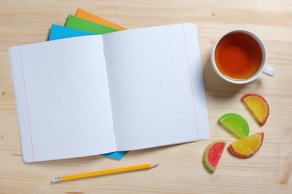 School notebooks, cup of tea and marmalade on dark wooden table, top view