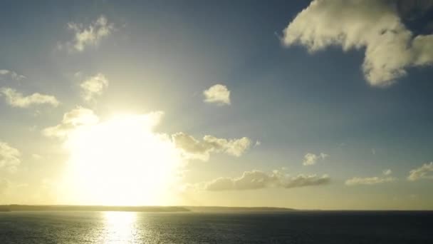 Wide shot of a sunset in timelapse over the ocean and cliffs on the horizon. Zooming progressively on the cliffs. Large space on a big sun, useful to place text or graphics. Small clouds are moving from the sun at horizon towards the foreground. — ストック動画