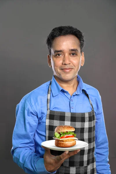 Indian Male Chef with a Burger in Hand on Grey Background