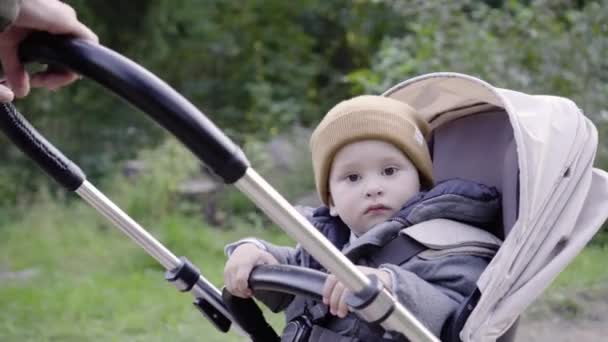 Mamma tar barnet i en barnvagn. Ett barn ser på kameran — Stockvideo