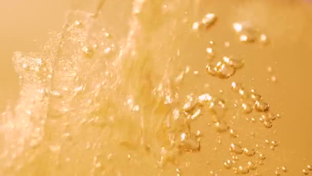 Sinaasappelvloeistof wordt in een glas gegoten. Veel opstijgende bellen — Stockvideo